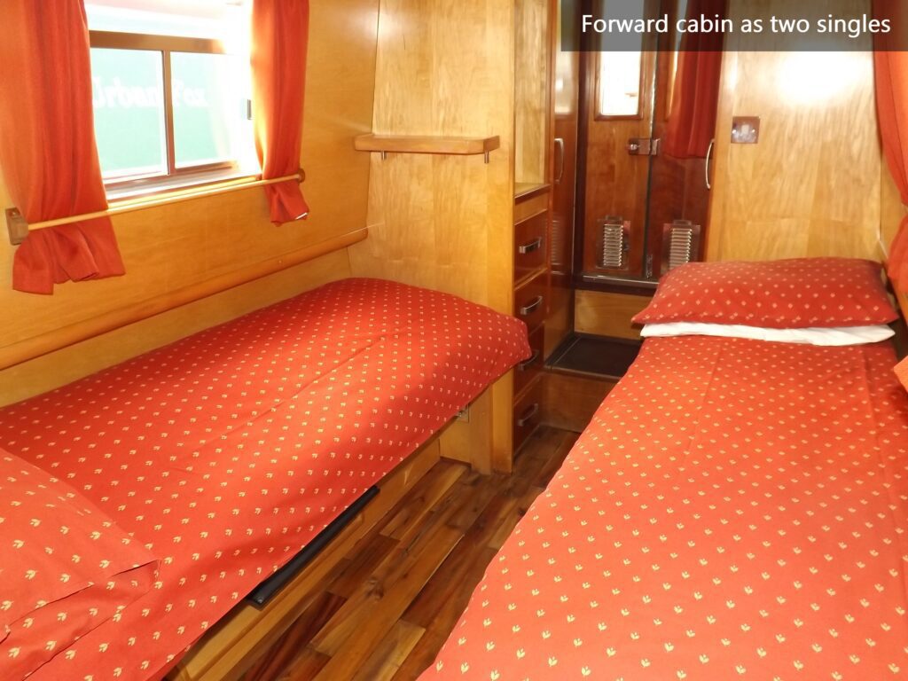 Middle cabin on WilyFox narrowboat with two single beds, wooden interior and red patterned bedding.