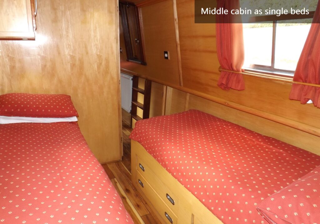 Middle cabin on WilyFox narrowboat with two single beds, wooden interior and red patterned bedding.